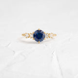 This engagement ring features 925 sterling silver with yellow gold plating, set with a deep blue round cut blue stone, exuding classic and noble elegance