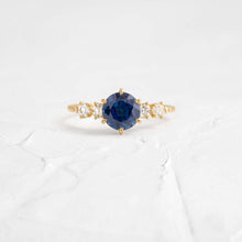 This engagement ring features 925 sterling silver with yellow gold plating, set with a deep blue round cut blue stone, exuding classic and noble elegance